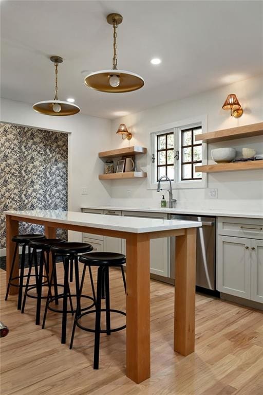 bar featuring light wood-type flooring, stainless steel dishwasher, gray cabinetry, sink, and decorative light fixtures