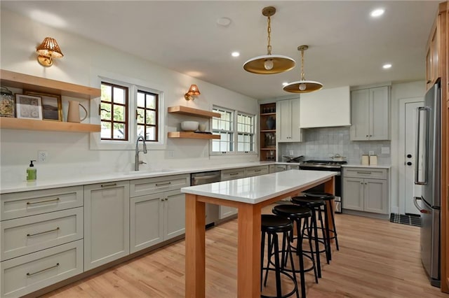 kitchen featuring decorative light fixtures, sink, light wood-type flooring, and stainless steel appliances