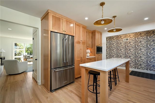 kitchen featuring a breakfast bar area, high end refrigerator, light brown cabinets, and light wood-type flooring