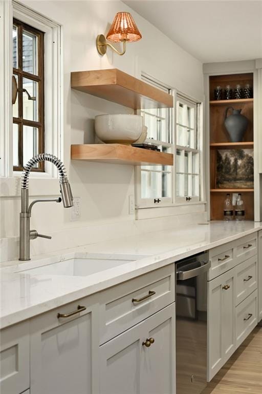 kitchen with stainless steel dishwasher, light stone countertops, sink, and light hardwood / wood-style flooring