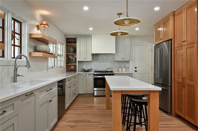 kitchen with a kitchen breakfast bar, sink, hanging light fixtures, light hardwood / wood-style floors, and stainless steel appliances