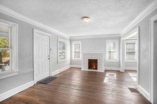 unfurnished living room featuring ornamental molding, dark hardwood / wood-style floors, a tiled fireplace, and a textured ceiling