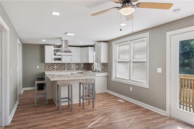 kitchen featuring white cabinetry, wall chimney range hood, hardwood / wood-style flooring, and plenty of natural light