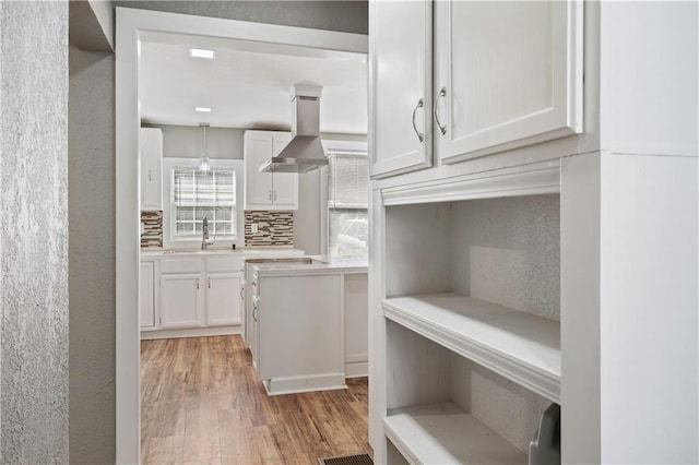 kitchen featuring wall chimney range hood, decorative backsplash, white cabinetry, light hardwood / wood-style flooring, and sink