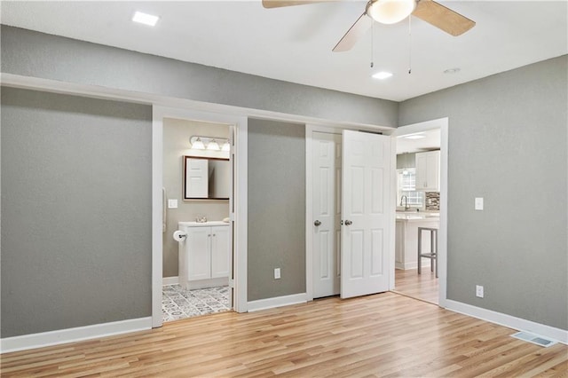 unfurnished bedroom featuring sink, ensuite bathroom, light hardwood / wood-style flooring, and ceiling fan