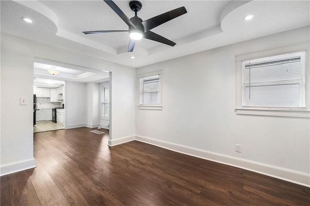 empty room featuring ceiling fan, a tray ceiling, and dark hardwood / wood-style flooring