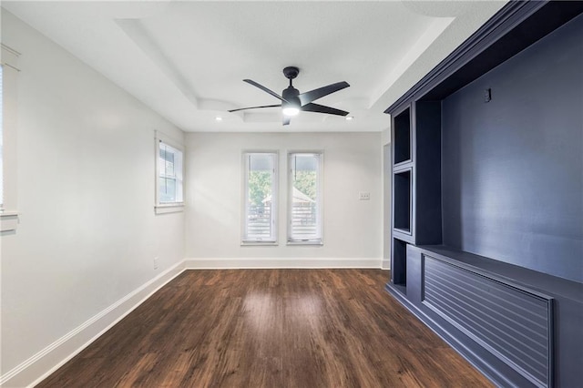 unfurnished living room with dark wood-type flooring, a raised ceiling, and ceiling fan