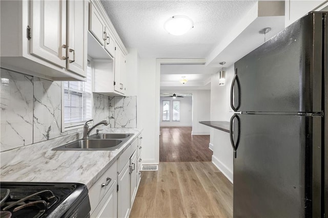 kitchen with tasteful backsplash, sink, fridge, white cabinets, and light hardwood / wood-style flooring