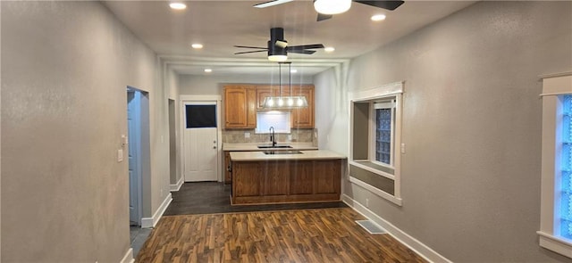 kitchen with kitchen peninsula, sink, hanging light fixtures, and dark hardwood / wood-style floors