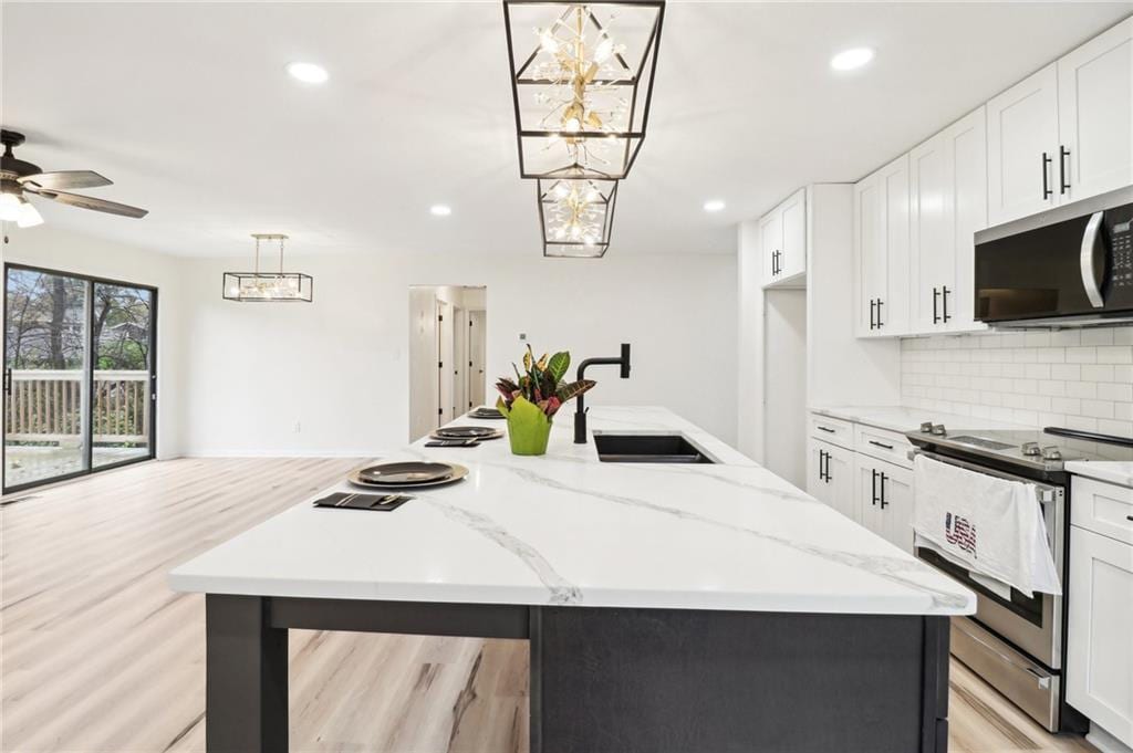 kitchen with white cabinetry, electric stove, hanging light fixtures, and an island with sink