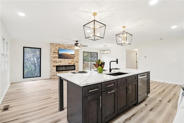 kitchen featuring ceiling fan, sink, a stone fireplace, decorative light fixtures, and a center island with sink