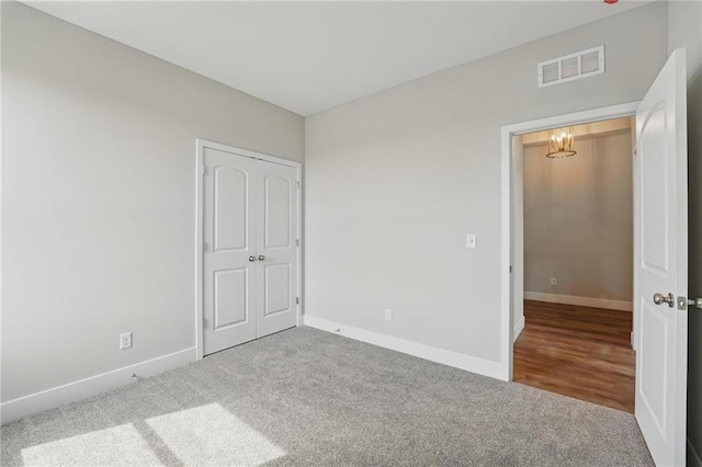 unfurnished bedroom featuring carpet floors, a chandelier, baseboards, and a closet
