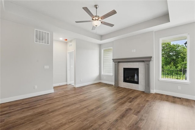 unfurnished living room featuring ceiling fan, wood finished floors, baseboards, a tile fireplace, and a tray ceiling