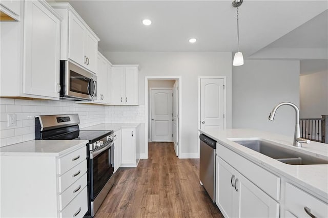 kitchen with stainless steel appliances, a sink, decorative backsplash, dark wood-style floors, and white cabinetry