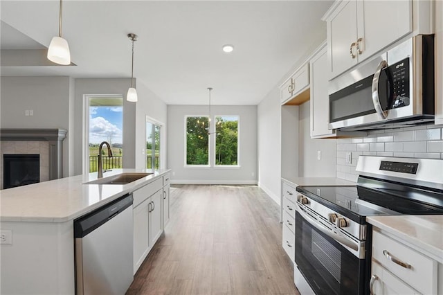 kitchen featuring appliances with stainless steel finishes, a sink, wood finished floors, white cabinetry, and tasteful backsplash