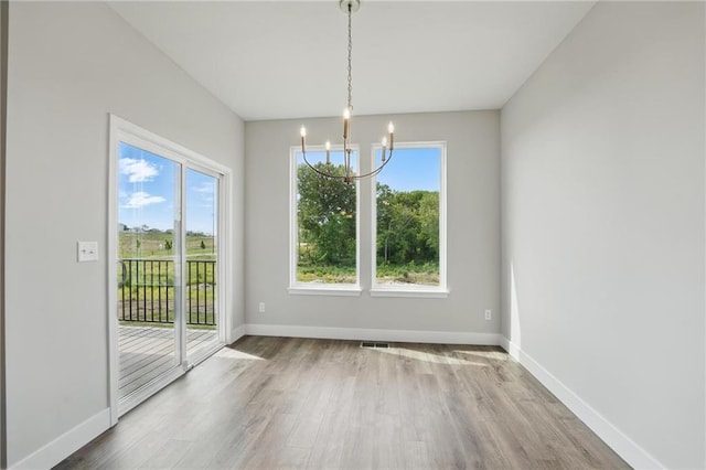 unfurnished dining area featuring a chandelier, wood finished floors, plenty of natural light, and baseboards