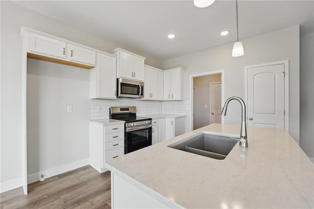kitchen featuring appliances with stainless steel finishes, a sink, light wood-style flooring, white cabinetry, and recessed lighting