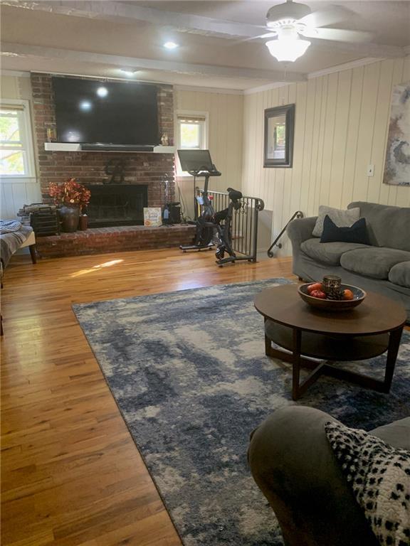 living room featuring hardwood / wood-style flooring, beam ceiling, a brick fireplace, and ceiling fan