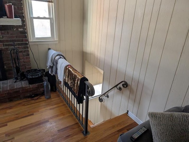 staircase with wood-type flooring, wooden walls, and a brick fireplace