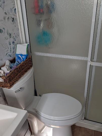 bathroom with tile patterned floors, toilet, and an enclosed shower