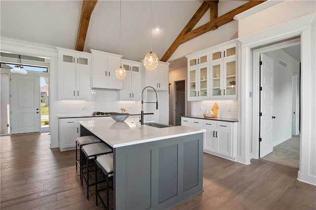 kitchen featuring beamed ceiling, sink, white cabinetry, and a kitchen island with sink