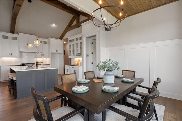 dining area featuring dark hardwood / wood-style floors, beam ceiling, sink, an inviting chandelier, and high vaulted ceiling