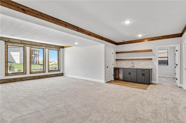 unfurnished living room with crown molding, indoor bar, and light colored carpet