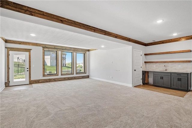 unfurnished living room featuring crown molding, a healthy amount of sunlight, light colored carpet, and sink