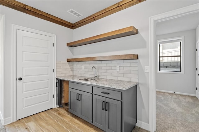 kitchen featuring light hardwood / wood-style flooring, gray cabinetry, sink, light stone countertops, and tasteful backsplash