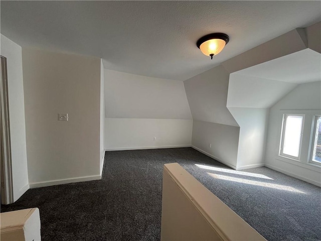 additional living space with dark carpet, vaulted ceiling, and a textured ceiling