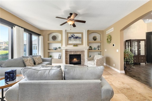 living room with ceiling fan, a textured ceiling, light hardwood / wood-style flooring, a fireplace, and built in features