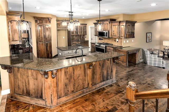 kitchen with sink, appliances with stainless steel finishes, decorative light fixtures, and dark hardwood / wood-style flooring