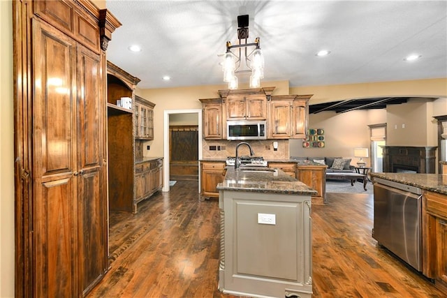 kitchen featuring sink, appliances with stainless steel finishes, dark hardwood / wood-style flooring, and a center island with sink