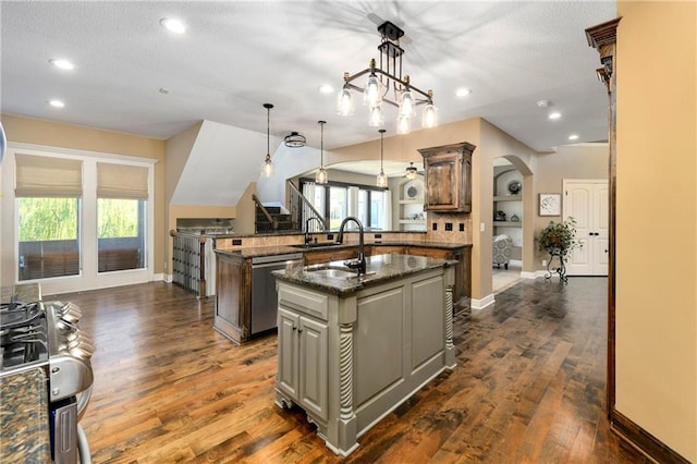 kitchen featuring dark stone counters, decorative light fixtures, stainless steel dishwasher, dark wood-type flooring, and a center island with sink