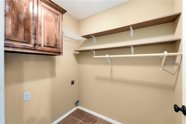 laundry room featuring dark tile patterned flooring, a textured ceiling, hookup for an electric dryer, and cabinets