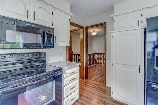 kitchen featuring light hardwood / wood-style flooring, white cabinetry, black appliances, and a textured ceiling