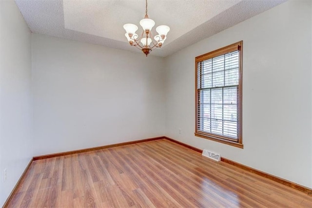 unfurnished room featuring an inviting chandelier, a textured ceiling, and wood-type flooring