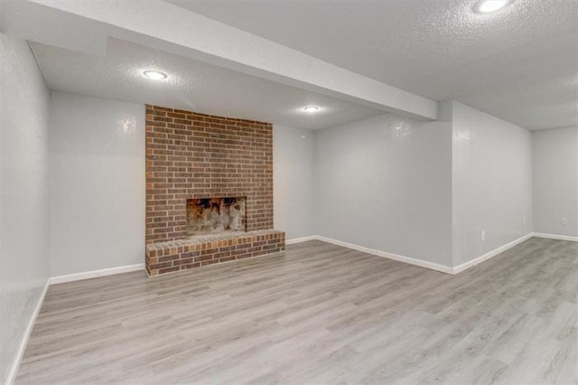 basement with a textured ceiling, light hardwood / wood-style flooring, and a fireplace