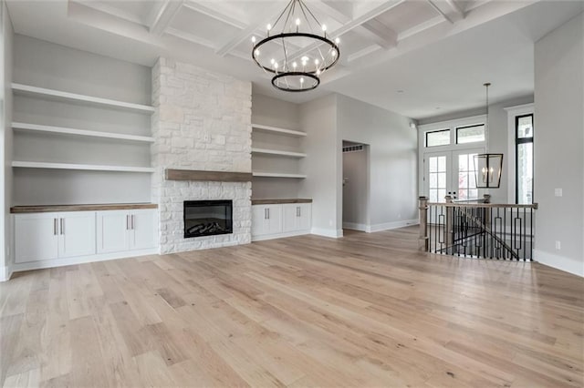 unfurnished living room featuring a notable chandelier, coffered ceiling, a fireplace, beamed ceiling, and light wood-type flooring