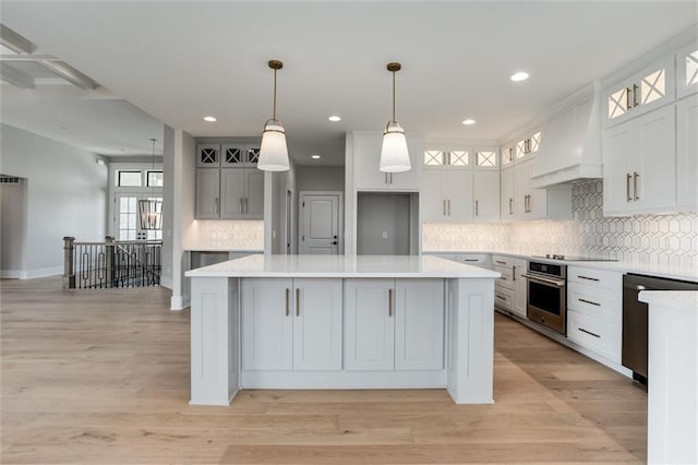 kitchen featuring light hardwood / wood-style floors, a center island, custom exhaust hood, appliances with stainless steel finishes, and decorative light fixtures