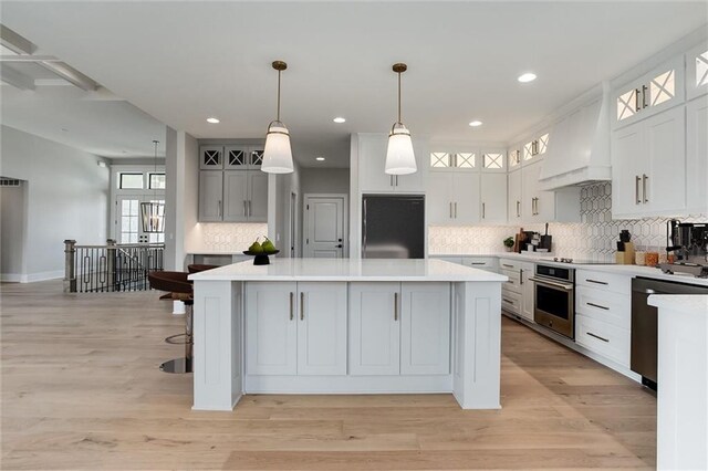 kitchen with premium range hood, stainless steel appliances, hanging light fixtures, white cabinets, and a center island