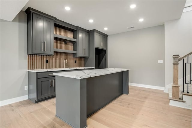 kitchen with gray cabinets, light hardwood / wood-style flooring, a center island, and backsplash