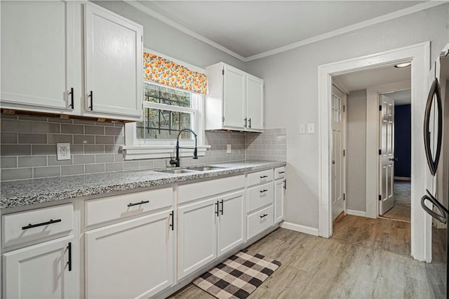 kitchen with white cabinets, tasteful backsplash, ornamental molding, light hardwood / wood-style floors, and sink