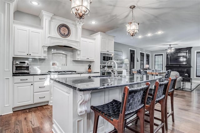 kitchen featuring ceiling fan with notable chandelier, dark wood-type flooring, hanging light fixtures, a breakfast bar area, and a kitchen island with sink