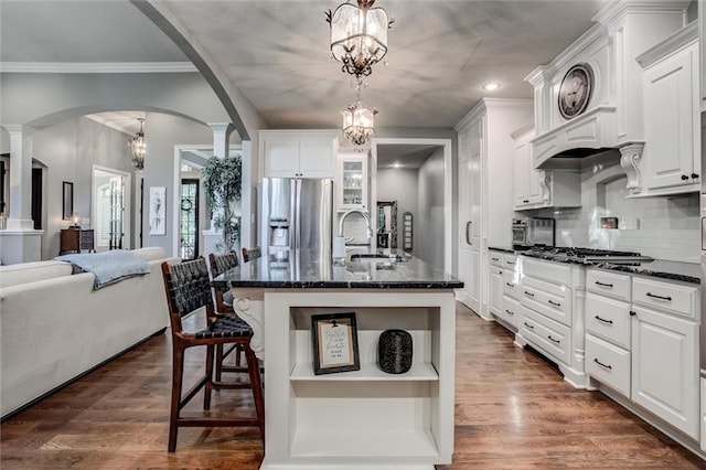 kitchen with a center island with sink, stainless steel appliances, white cabinetry, pendant lighting, and dark wood-type flooring