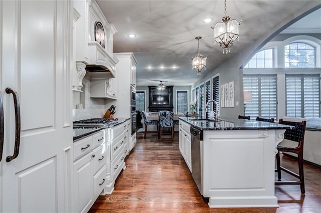 kitchen with stainless steel appliances, hanging light fixtures, an island with sink, white cabinets, and dark wood-type flooring