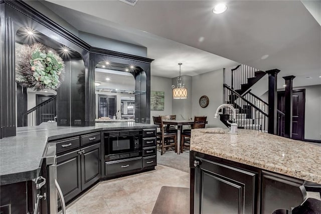 kitchen with ornate columns, black microwave, sink, a kitchen island with sink, and pendant lighting