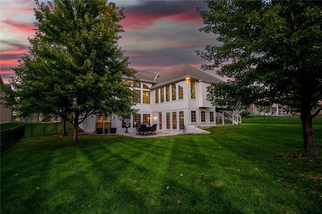 back house at dusk featuring a lawn, french doors, and a patio area