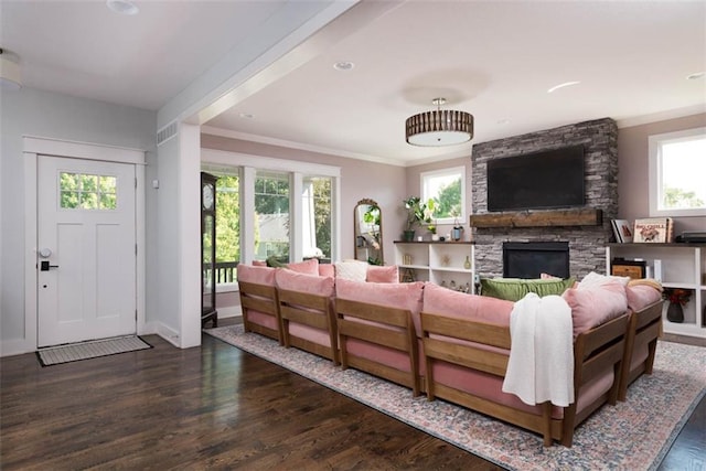 living room with ornamental molding, dark wood-type flooring, a stone fireplace, and a healthy amount of sunlight