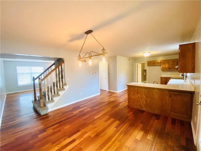 kitchen with hanging light fixtures, sink, kitchen peninsula, and dark hardwood / wood-style floors